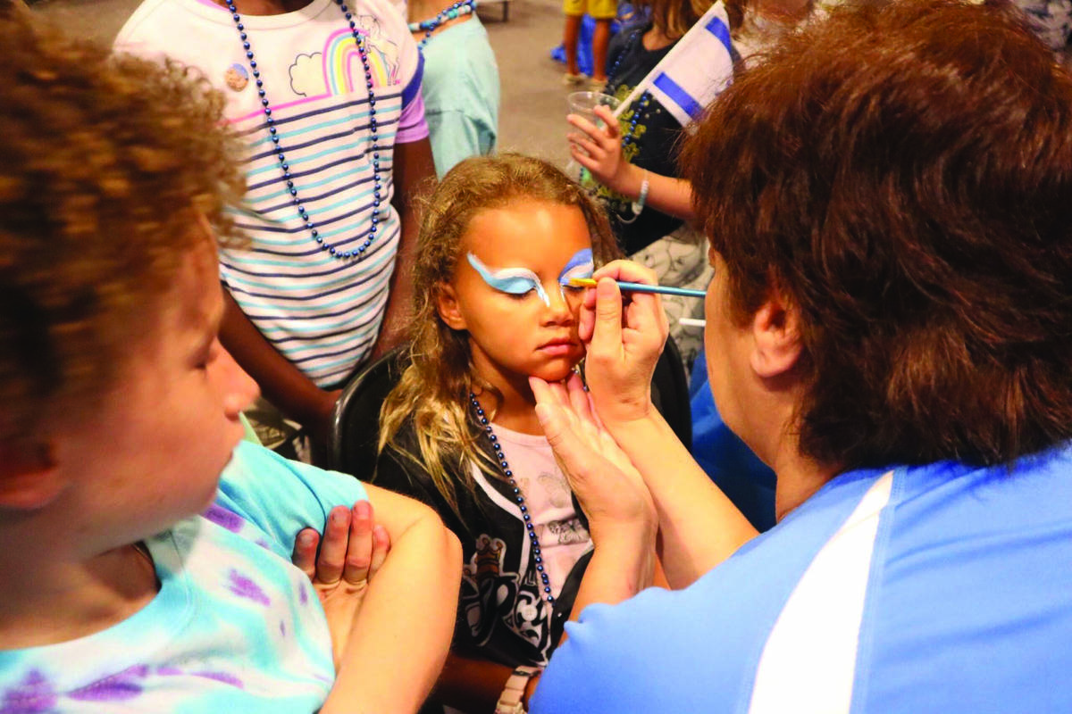 Sharon Serbin paints a camper’s face at Camp JCC’s Israel Day.